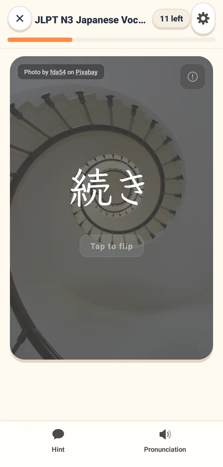 The front of a flashcard with a contextual photo background and a large Japanese word in the center. A tap to flip hint is below, and the plan name and remaining cards are at the top.